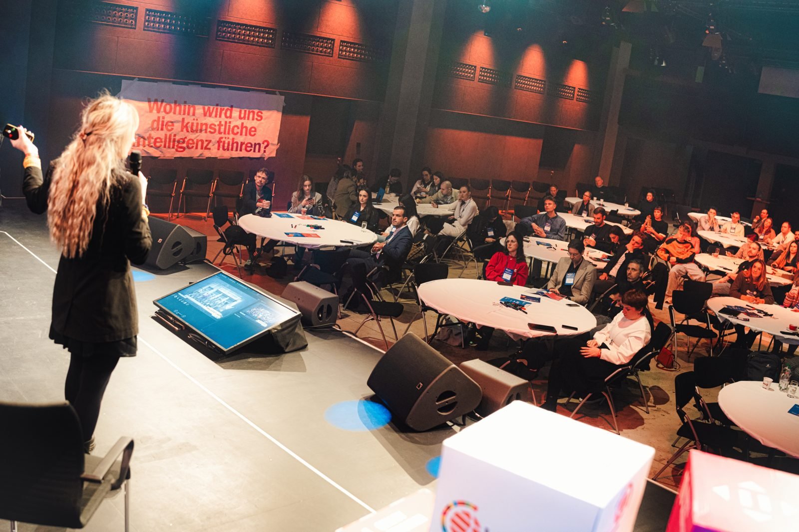 Odeta on stage at the European Young Innovators Festival 2024, facing an audience seated at round tables.